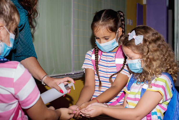 Діти в масках обробляють руки антисептиком 
