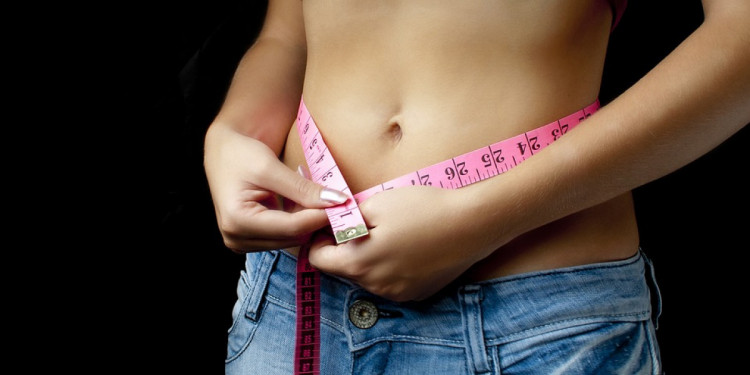 Дівчина заміряє талію сантиметром після схуднення 
