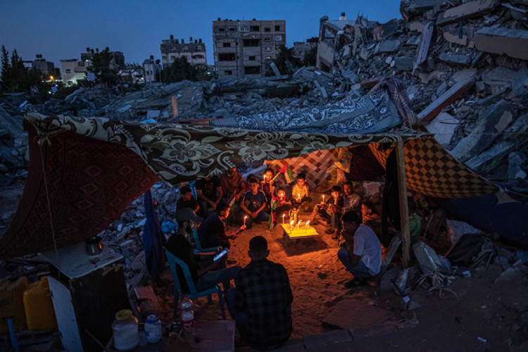Палестинские дети держат свечи во время митинга среди развалин домов, разрушенных израильскими авиаударами