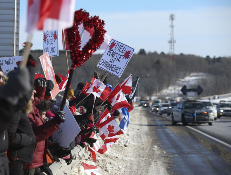 поклонники держат флаги, когда колонна грузовиков проходит по шоссе в Риго, Квебек. "Конвой свободы"
